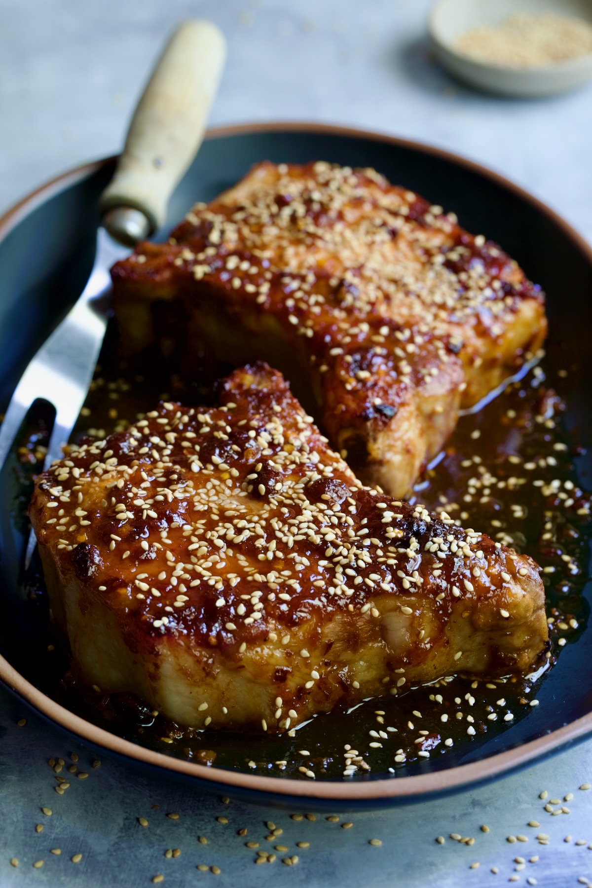 Two Asian Pork Chops on black oval platter garnished with sesame seeds.