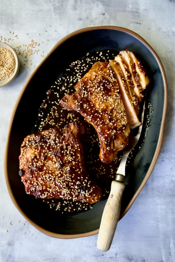 Two Asian Pork Chops on black oval platter garnished with sesame seeds with one pork chop partially sliced.