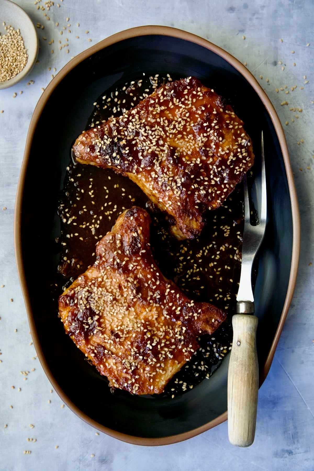 Two Asian Pork Chops on black oval platter garnished with sesame seeds.