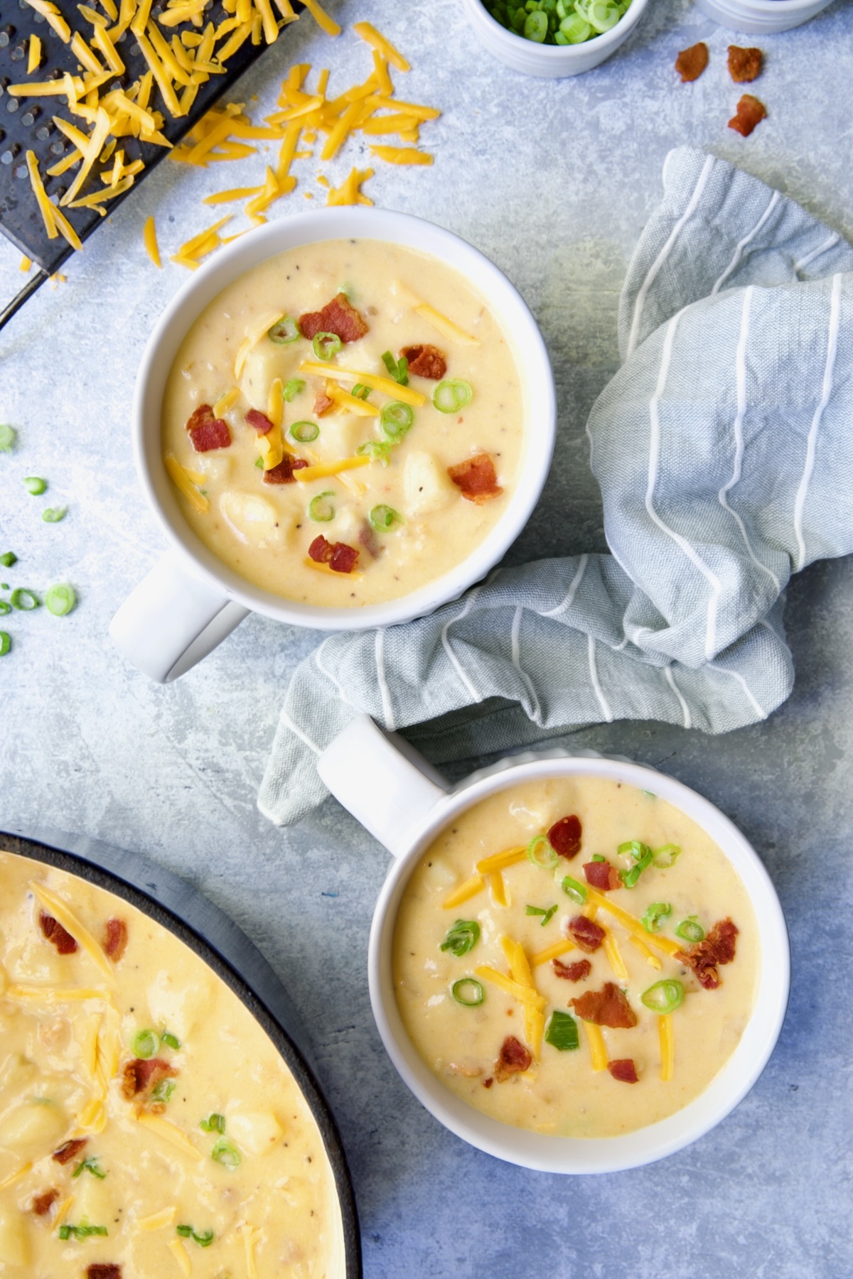 Two large soup mugs of Cheddar Bacon Potato Soup garnished with bacon and scallion.