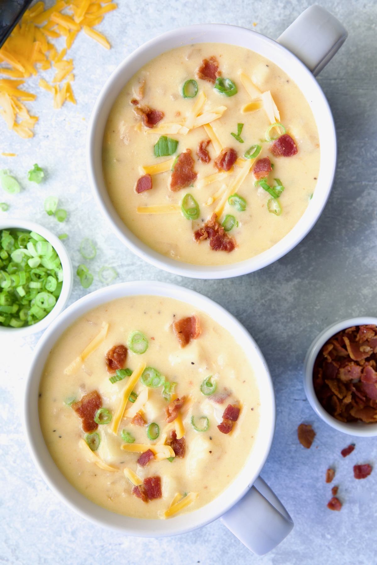 Two large soup mugs of Cheddar Bacon Potato Soup garnished with bacon and scallion.