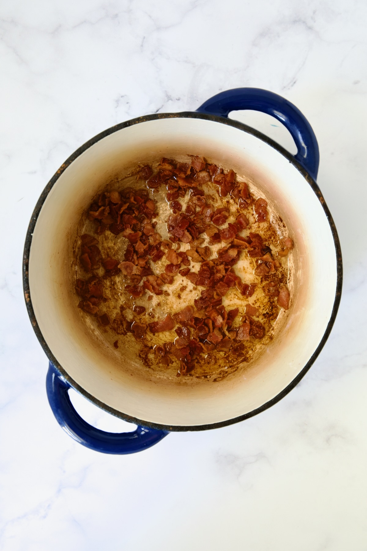 Browned bacon in blue Dutch oven.
