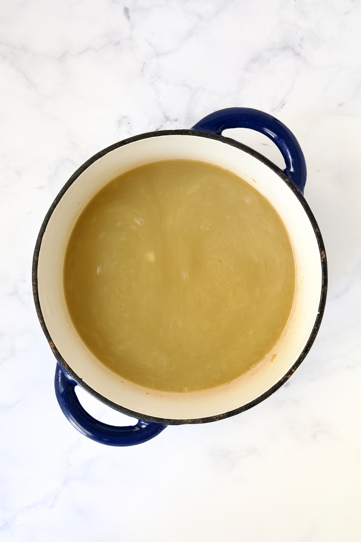 Chicken broth added to blue Dutch oven.