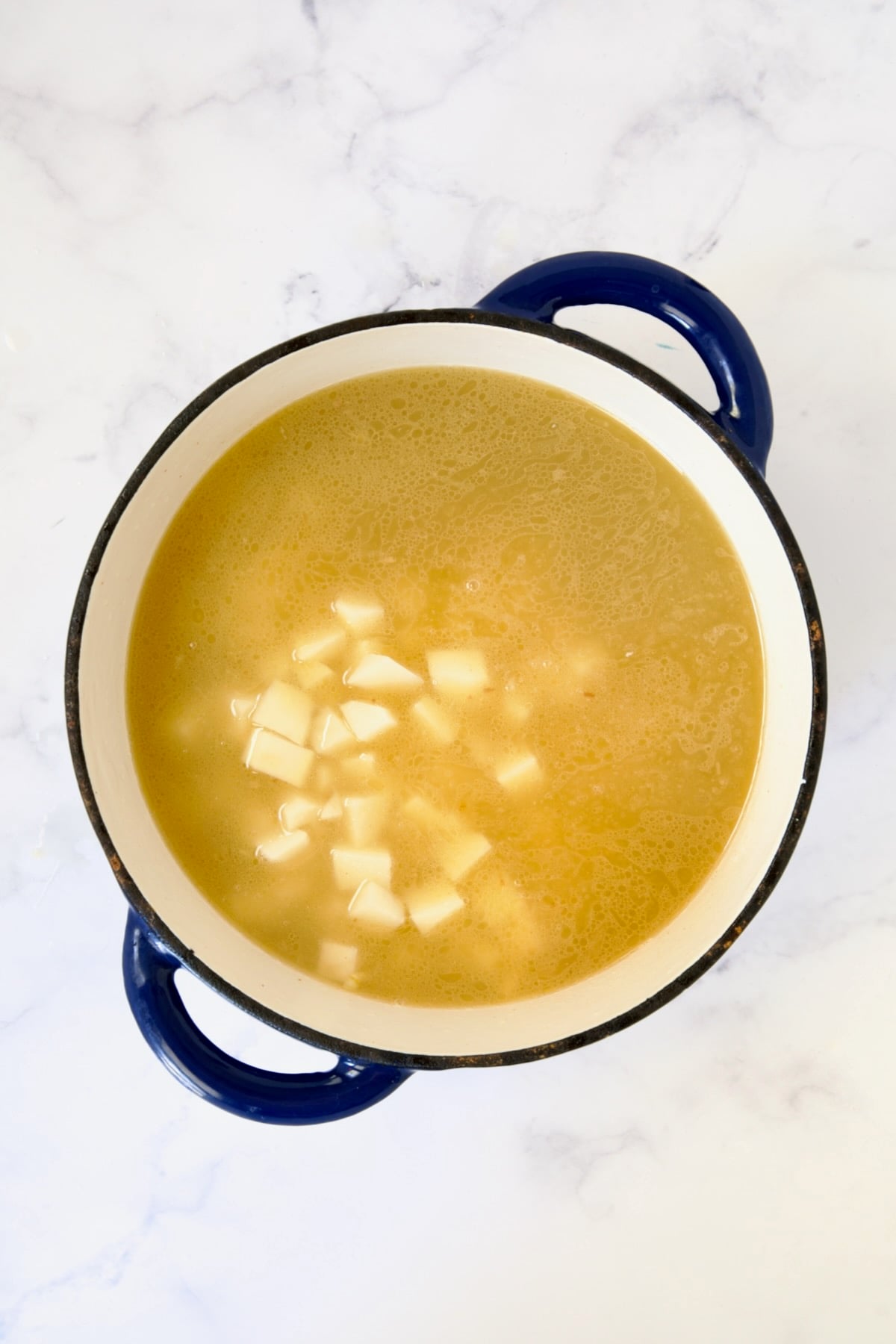 Potatoes added to broth in blue Dutch oven.