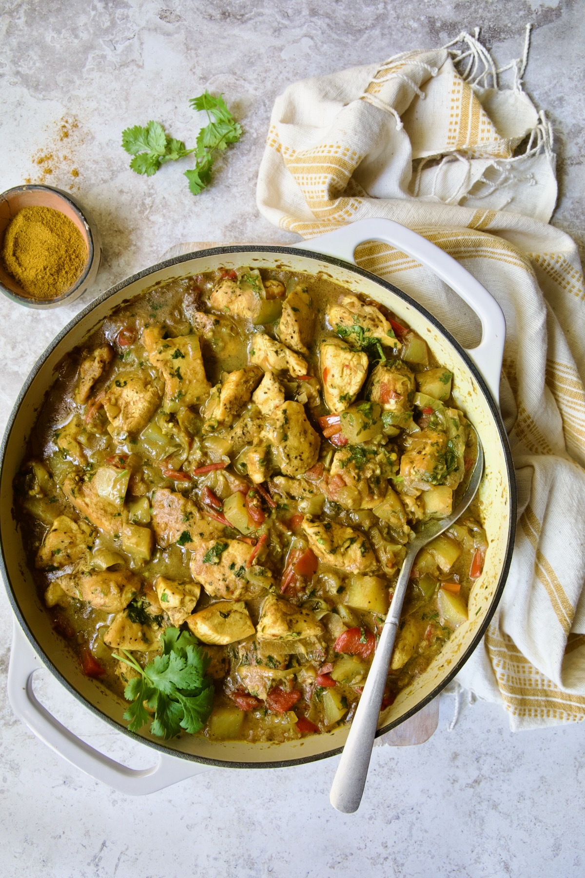 Chicken and Potato Curry in white enamel cast iron skillet with serving spoon.