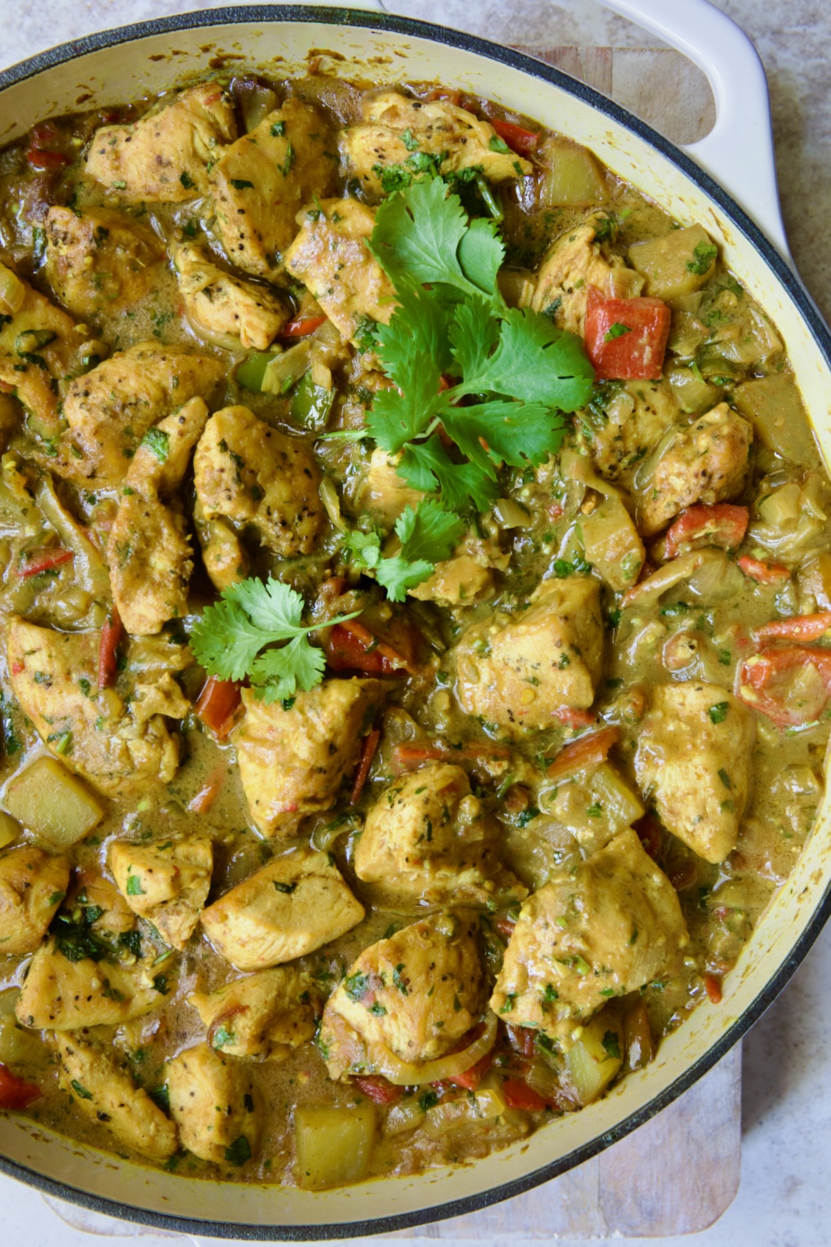 Chicken and Potato Curry in white enamel cast iron skillet with serving spoon garnished with fresh cilantro.