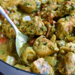Spoon scooping out some Chicken and Potato Curry from white enamel cast iron skillet.