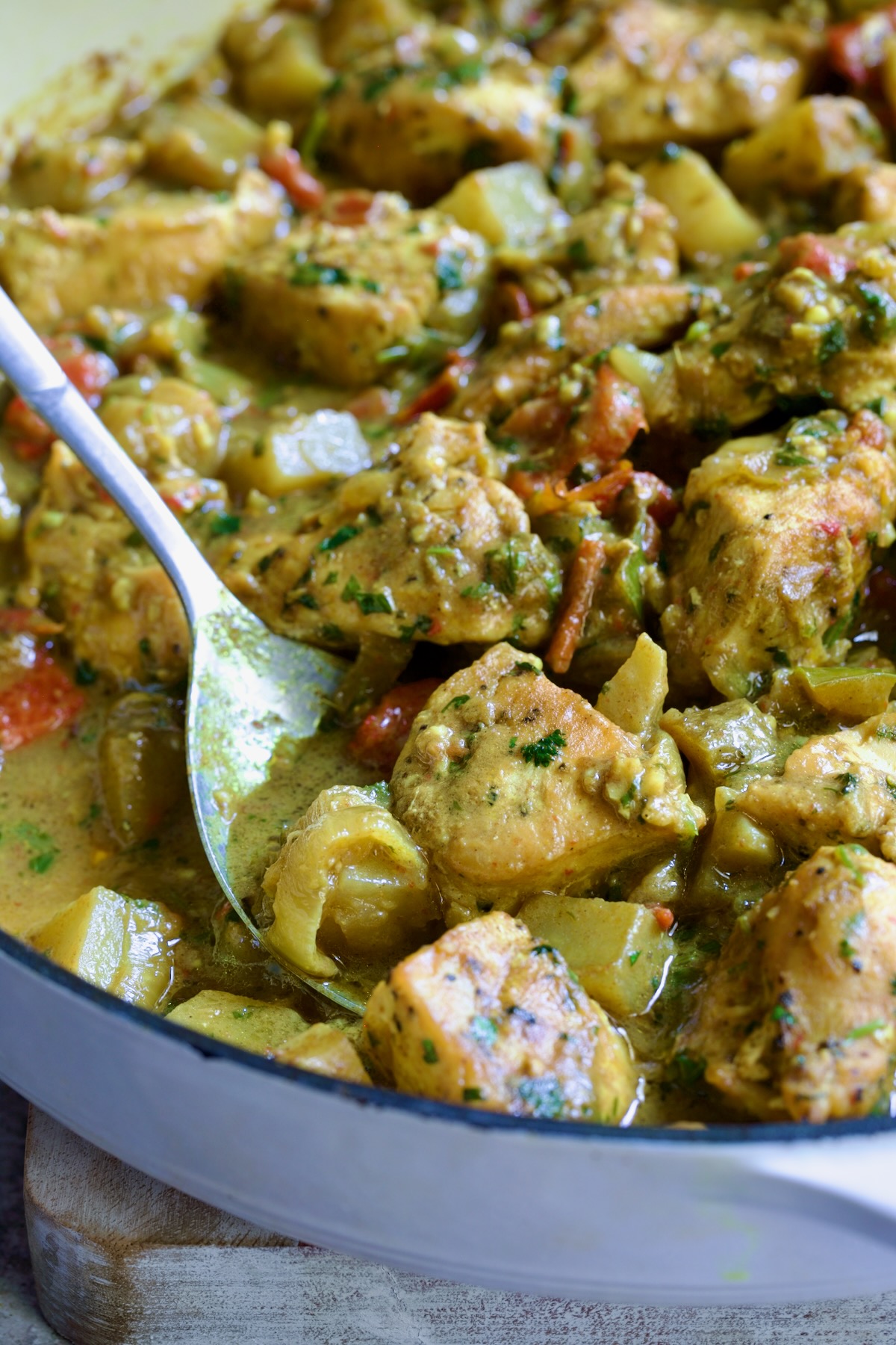 Spoon scooping out some Chicken and Potato Curry from white enamel cast iron skillet.