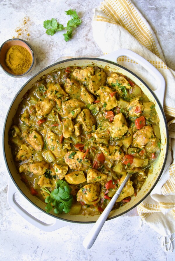 Chicken and Potato Curry in white enamel cast iron skillet with serving spoon.