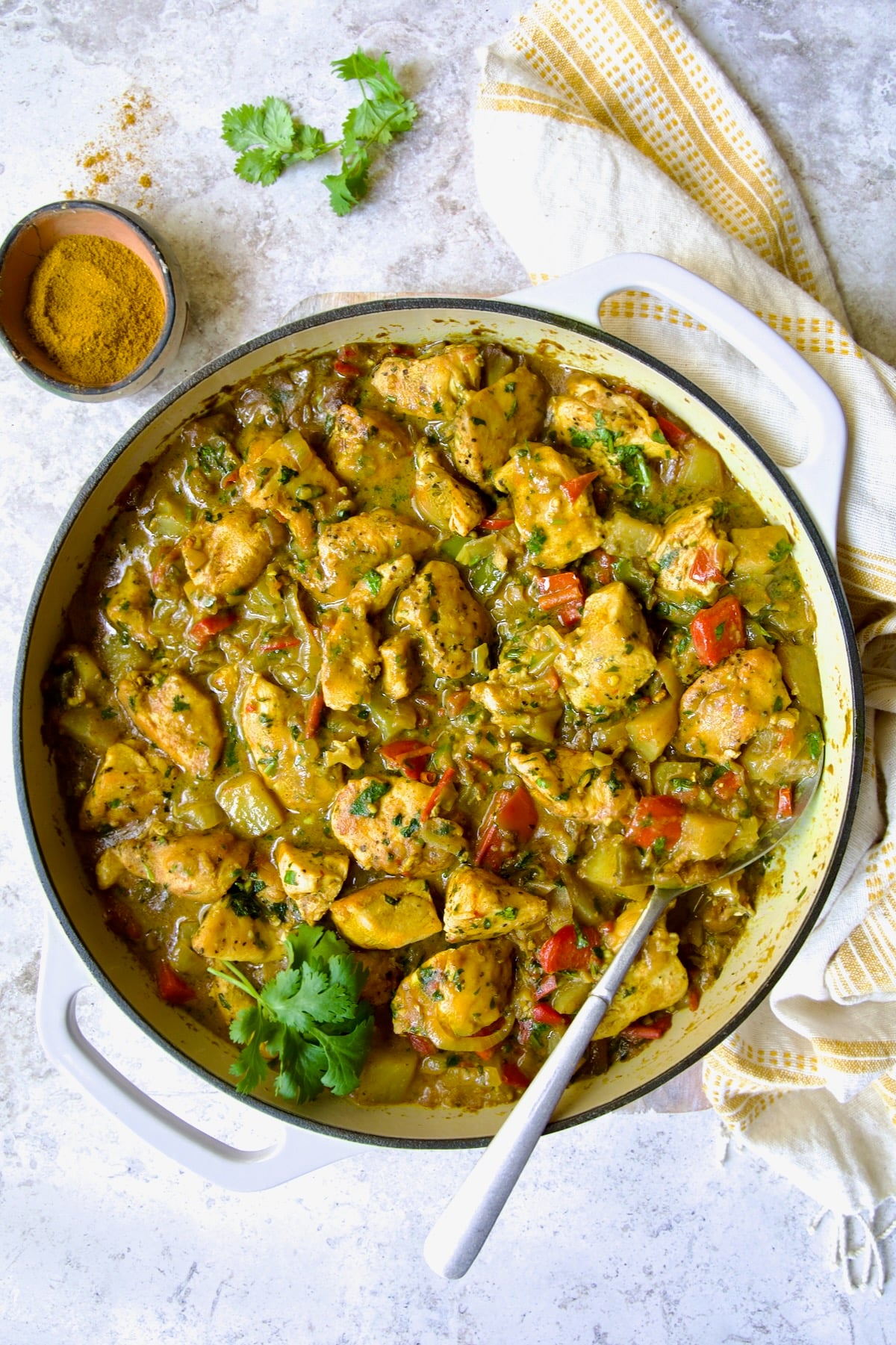 Chicken and Potato Curry in white enamel cast iron skillet with serving spoon.