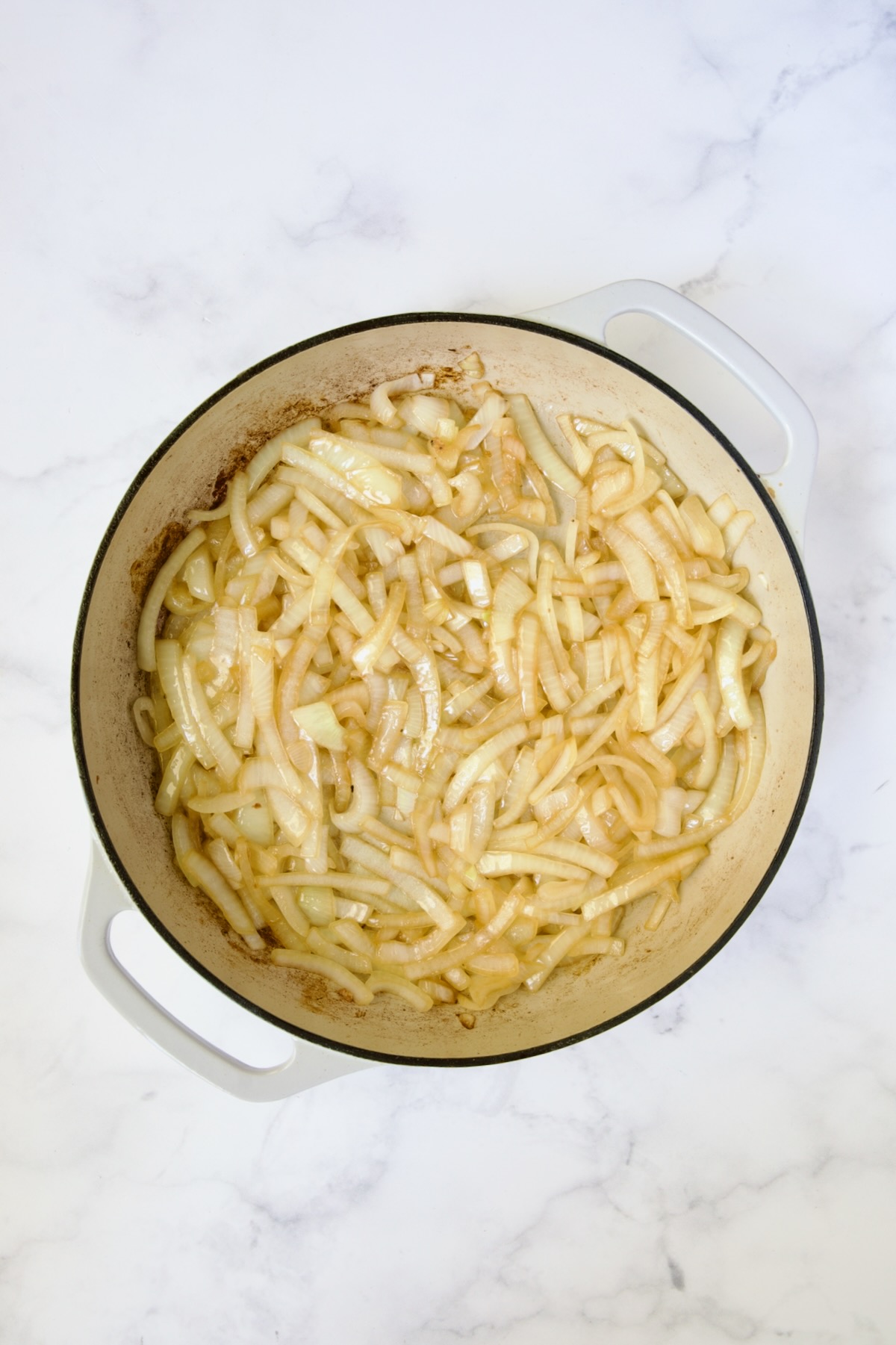 Lightly cooked onions in white enamel cast iron skillet.