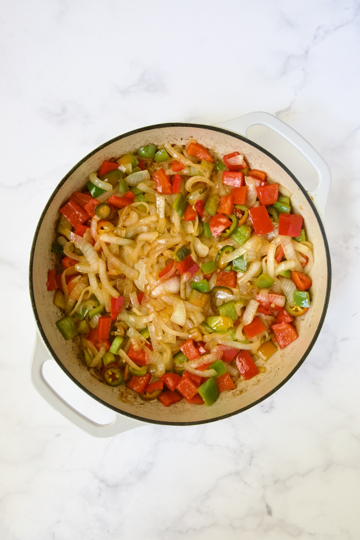 Cooked onions, red bell pepper, green bell pepper and jalapenos in white enamel cast iron skillet.