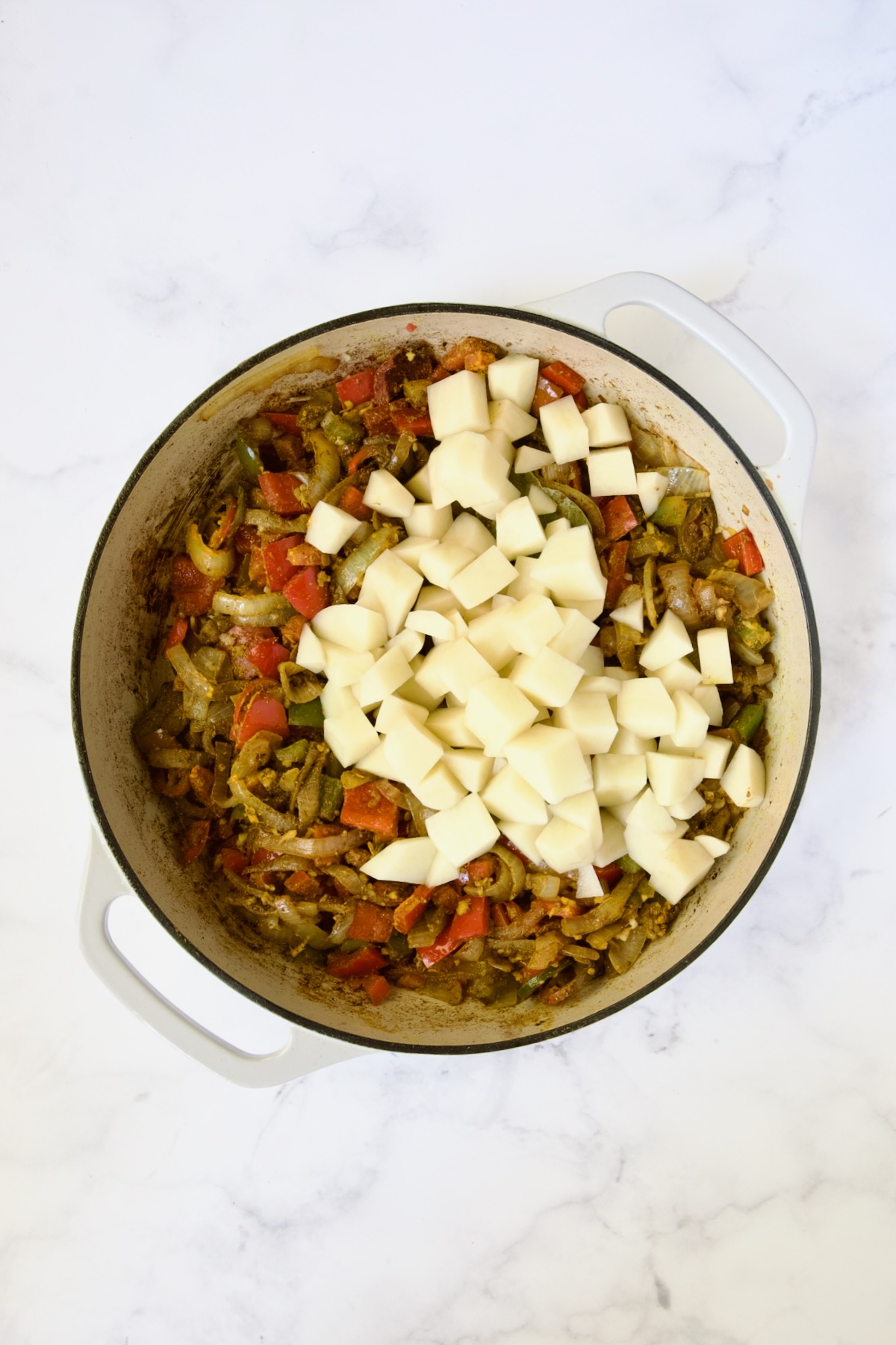 Potatoes added to onions, peppers and spices but not yet cooked.