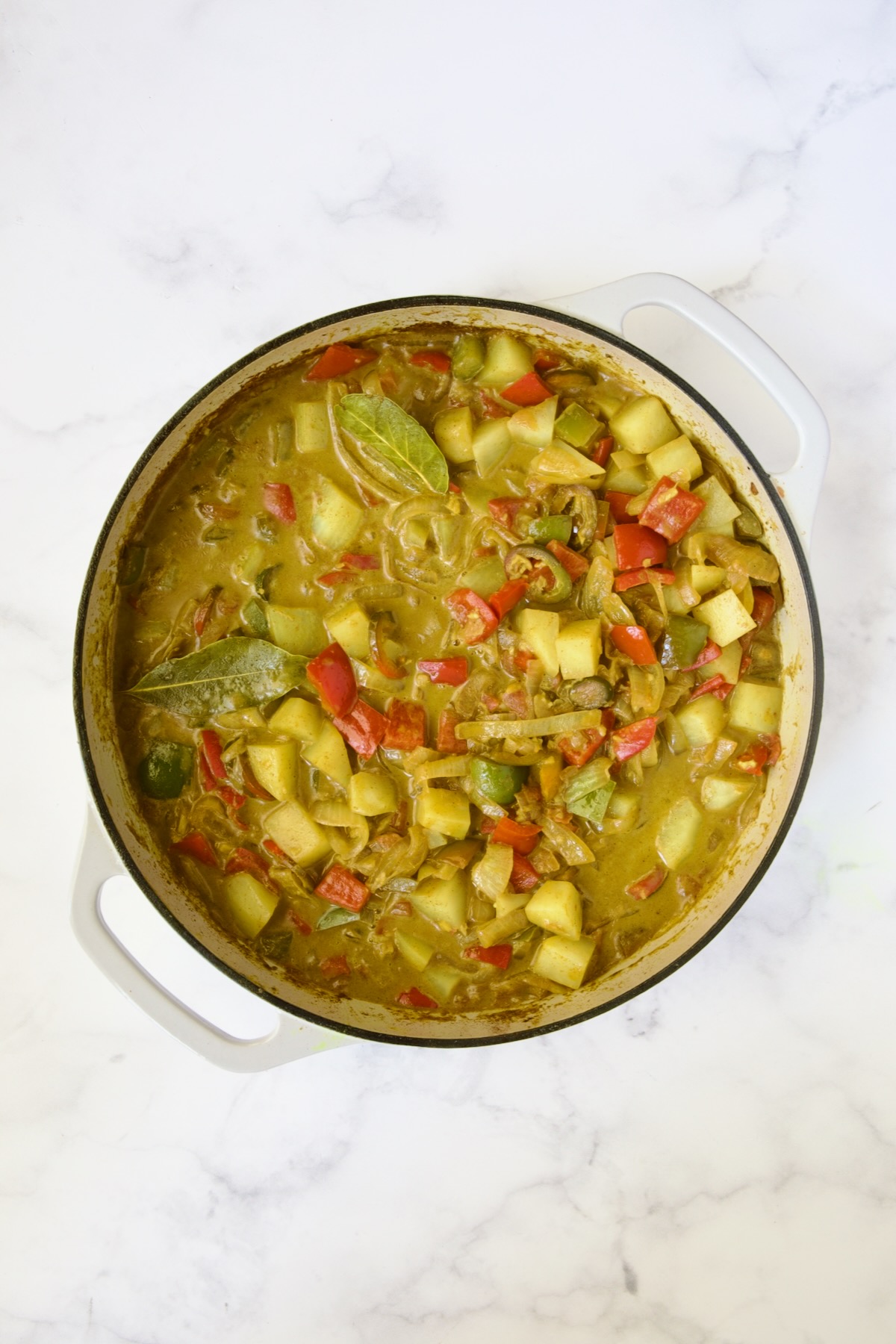 Cooked potatoes, peppers and onions in white enamel cast iron skillet.