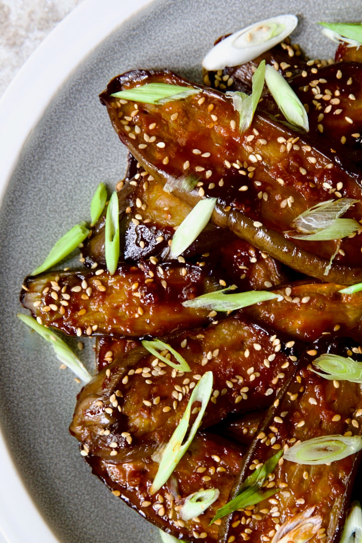 Gochujang Eggplant on round gray plate with white rim garnished with scallions and sesame seeds.
