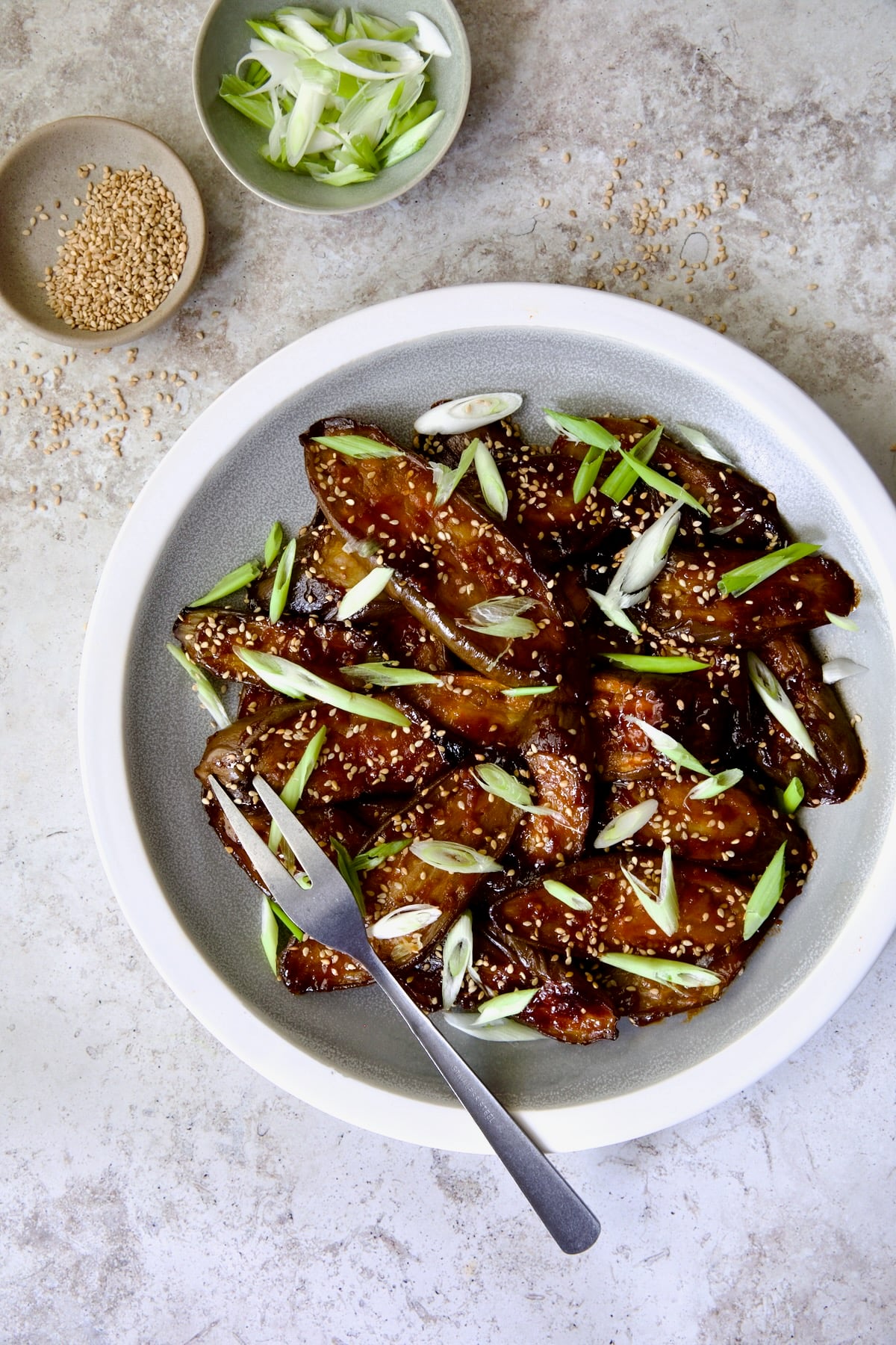 Gochujang Eggplant on round gray plate with white rim garnished with scallions and sesame seeds.
