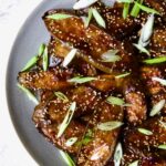 Gochujang Eggplant on round gray plate with white rim garnished with scallions and sesame seeds.