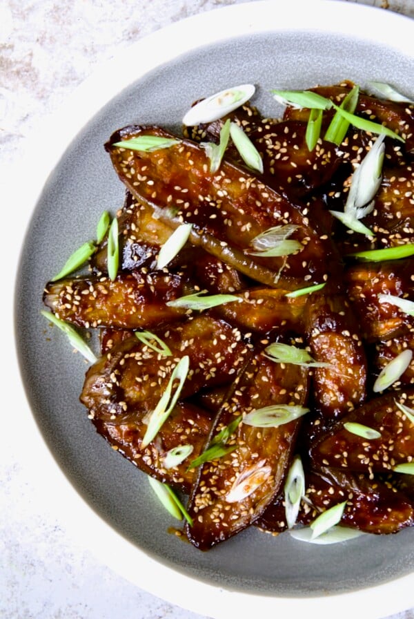 Gochujang Eggplant on round gray plate with white rim garnished with scallions and sesame seeds.