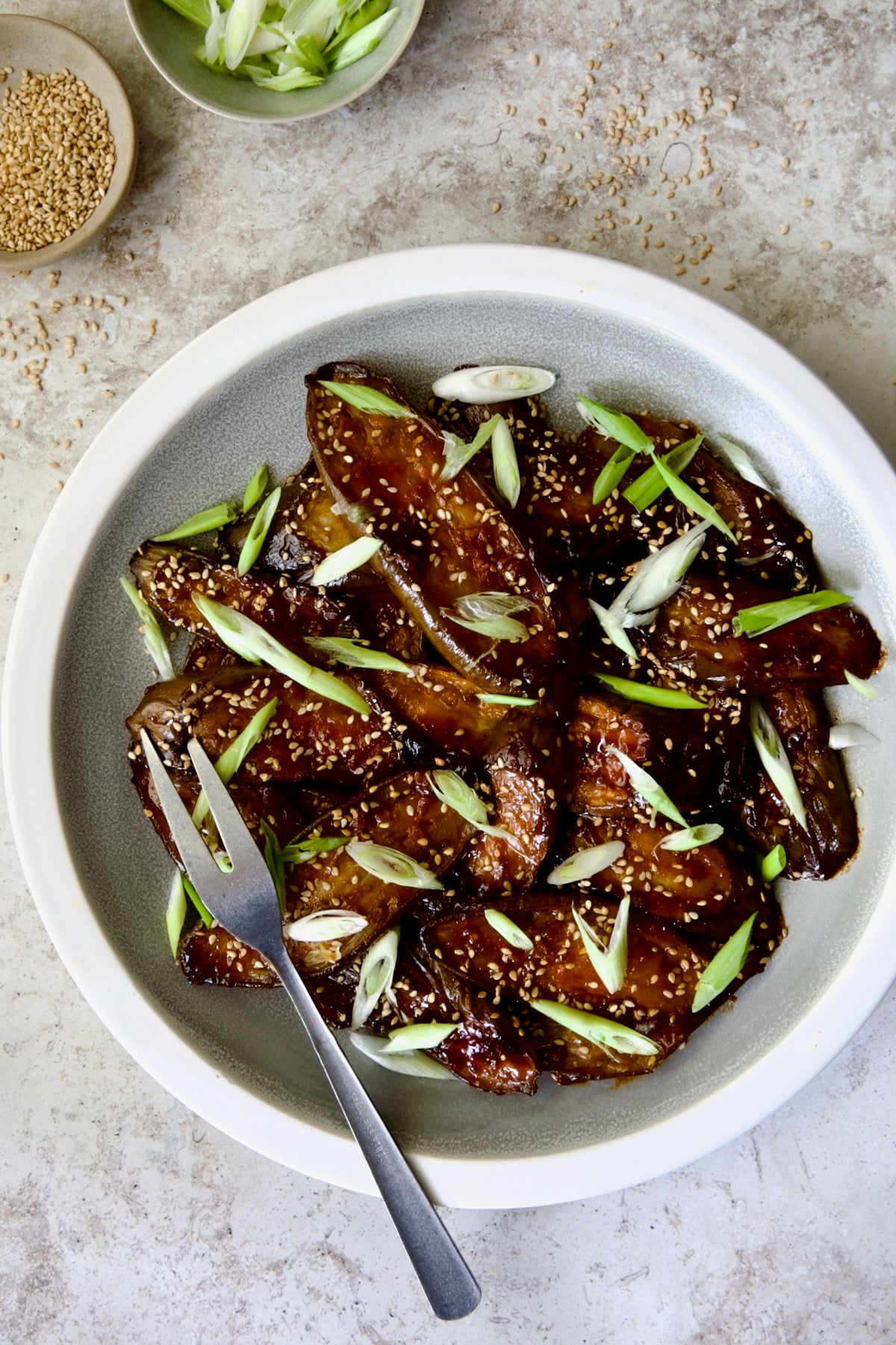 Gochujang Eggplant on round gray plate with white rim garnished with scallions and sesame seeds with serving fork.