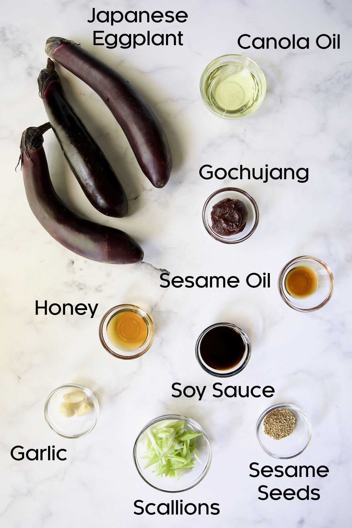 Ingredients for Gochujang Eggplant in glass bowls on marble surface.