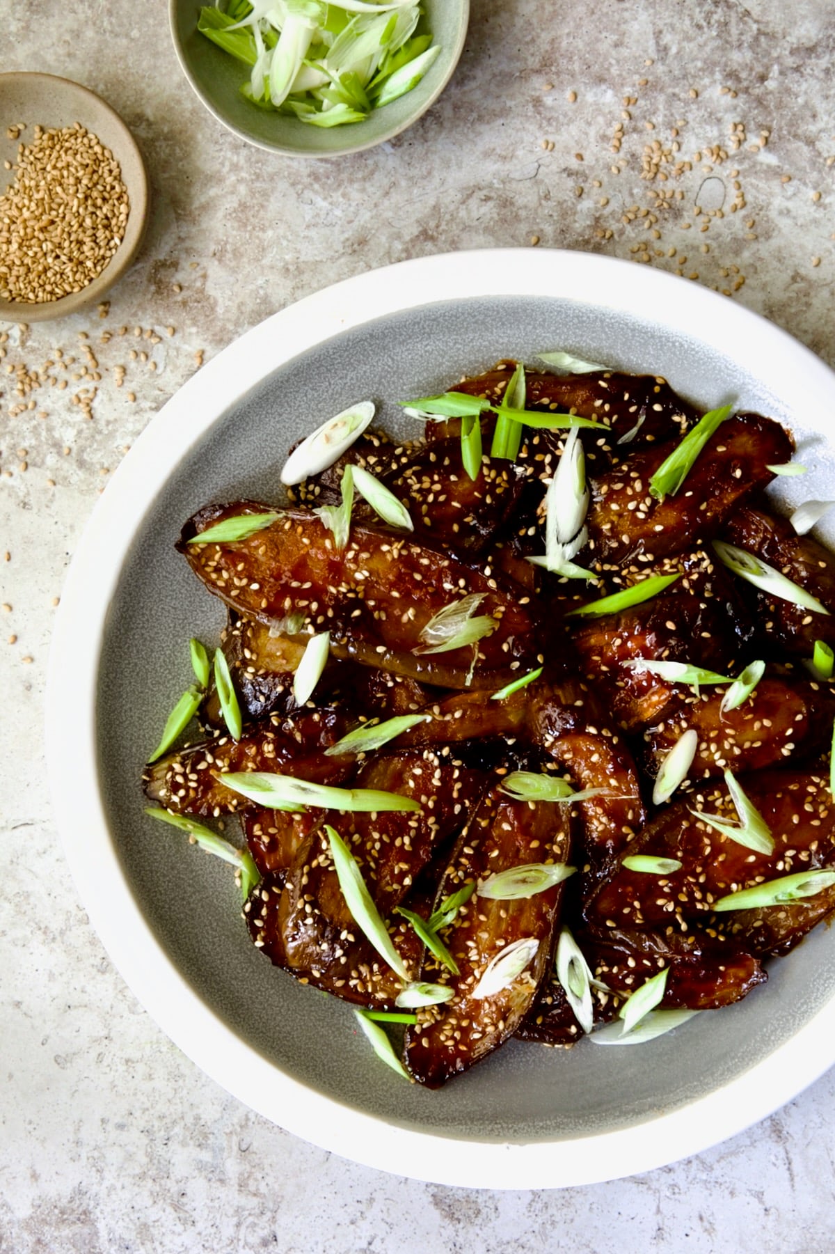 Gochujang Eggplant on round gray plate with white rim garnished with scallions and sesame seeds.