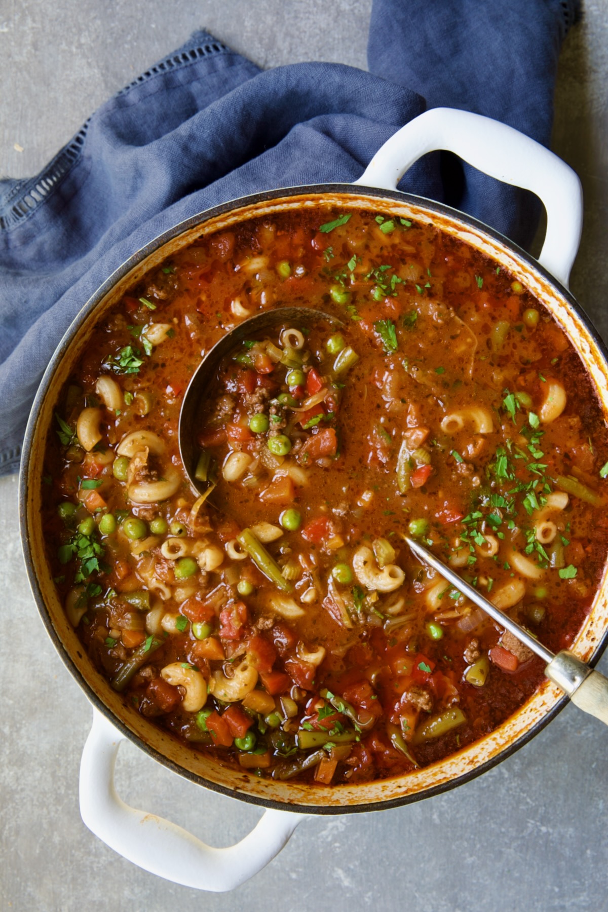 Hamburger Vegetable Soup in white Dutch oven with soup ladle and blue napkin.