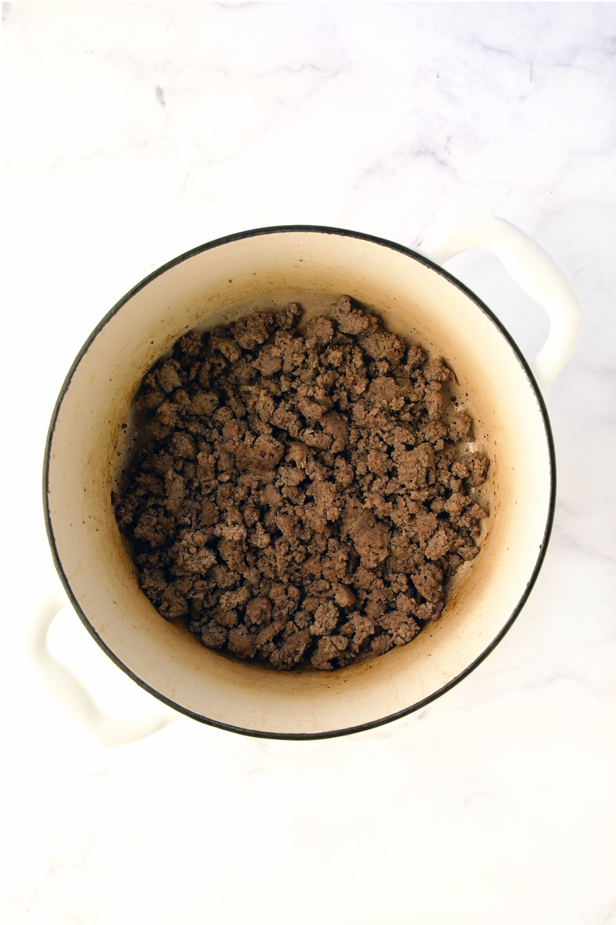 Cooked ground beef in white Dutch oven.