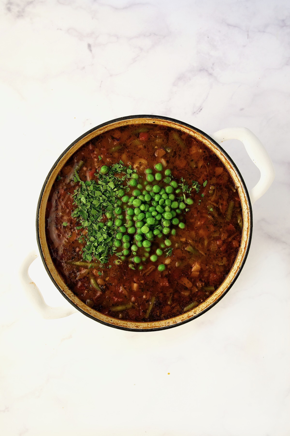 Peas and parsley added to soup in process in white Dutch oven.