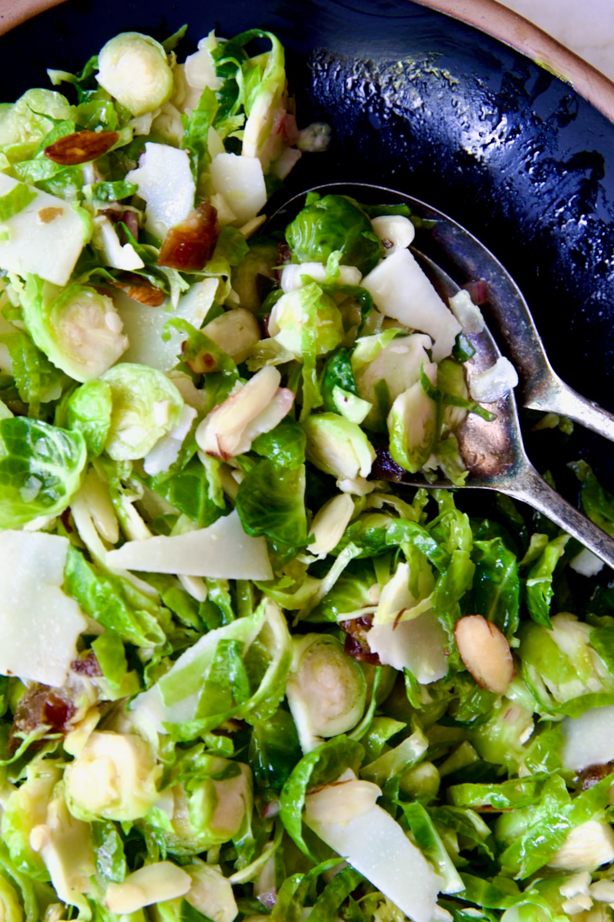 Shaved Brussels Sprouts Salad on a black platter with brown rim being scooped up with serving utensils.