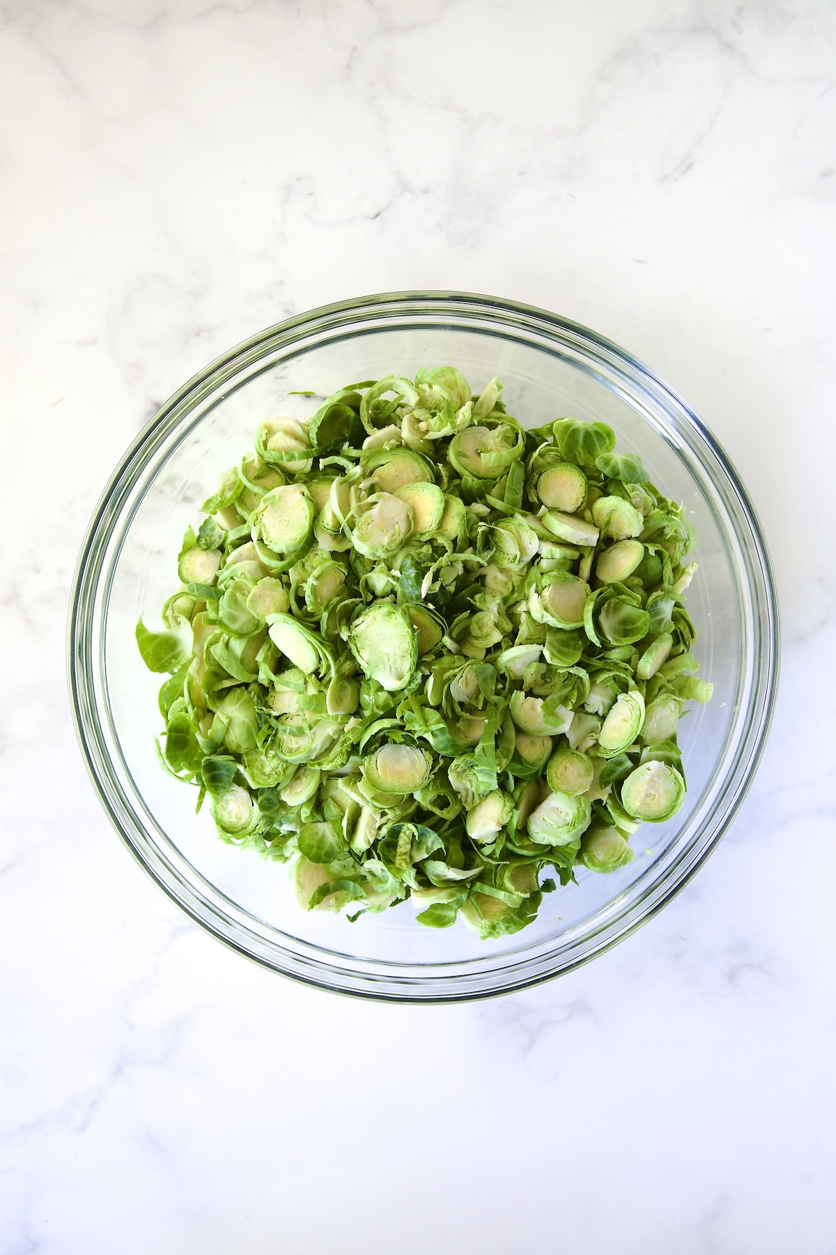 Thinly sliced (shaved) Brussels sprouts in glass bowl.