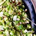 Shaved Brussels Sprouts Salad on black platter with brown rim and serving utensils.