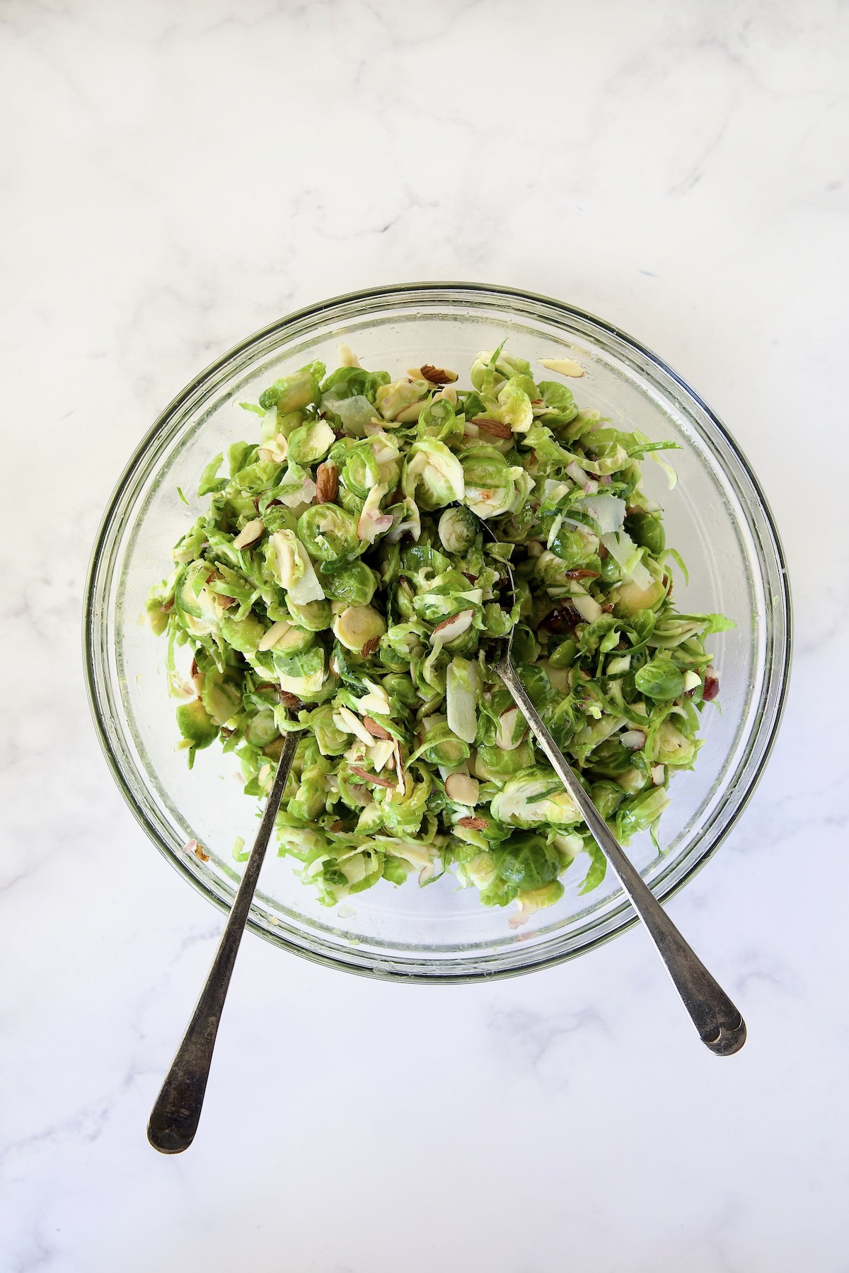 Shaved Brussels Sprouts Salad being mixed together in glass bowl.