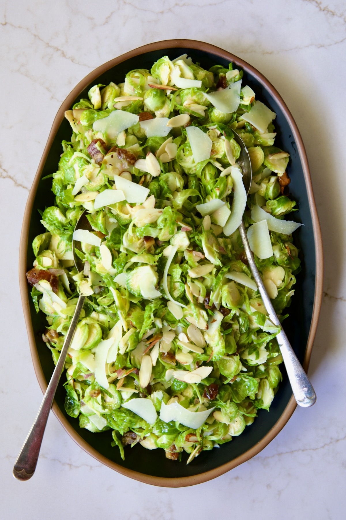 Shaved Brussels Sprouts Salad on black platter with brown rim with serving utensils.