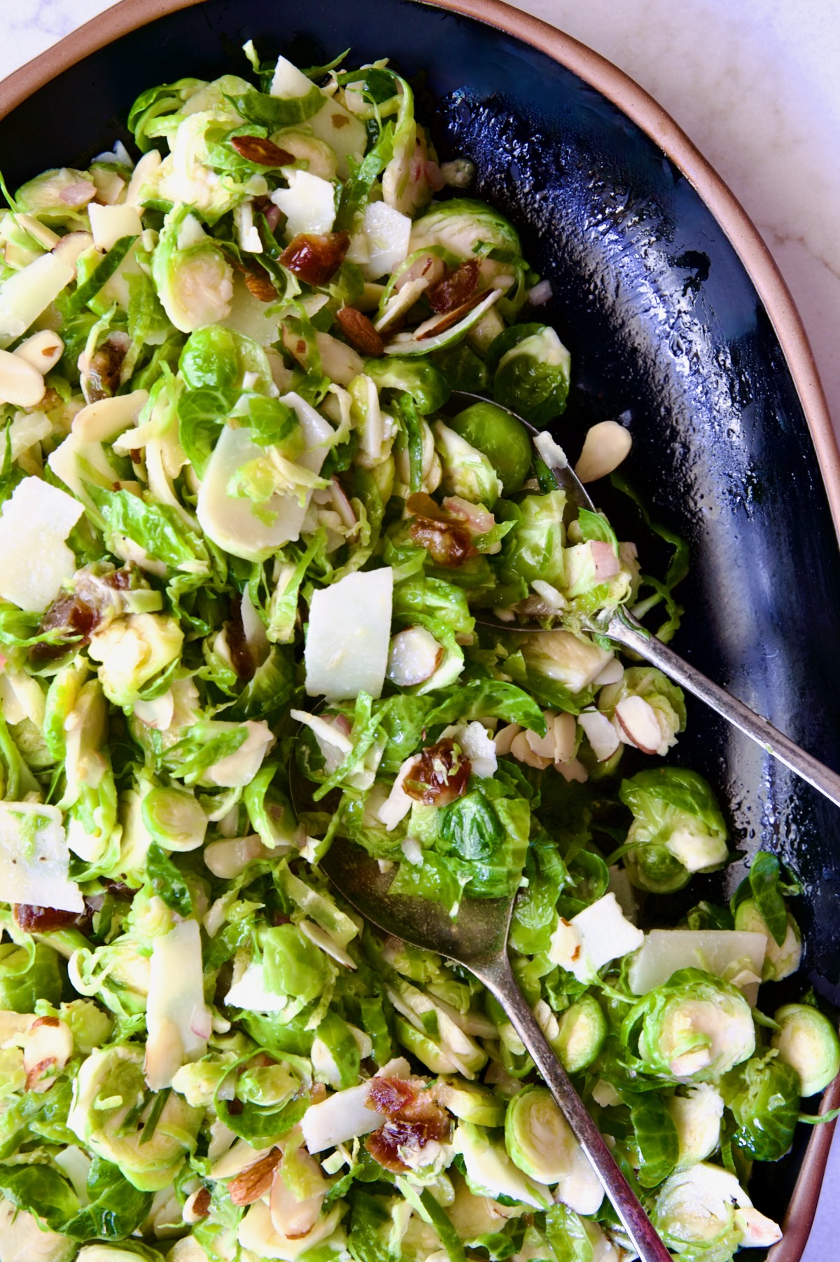 Shaved Brussels Sprouts Salad on black platter with brown rim and serving utensils.
