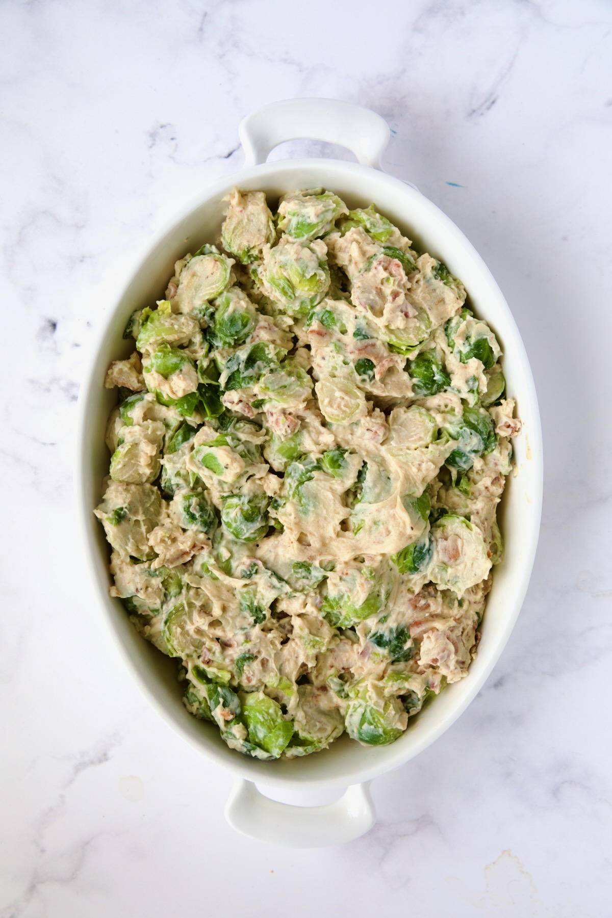 Brussels sprouts in cheese sauce are transferred to an oval baking dish.
