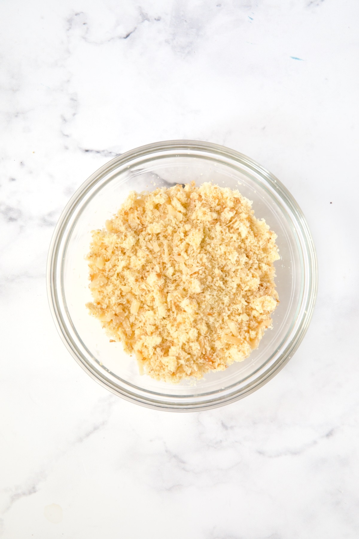 Breadcrumbs, cheese and butter mixed together in glass bowl.