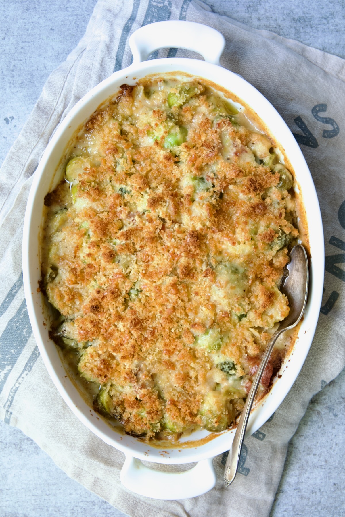 Fully baked Brussels Sprouts Gratin on a blue striped towel with a serving spoon.