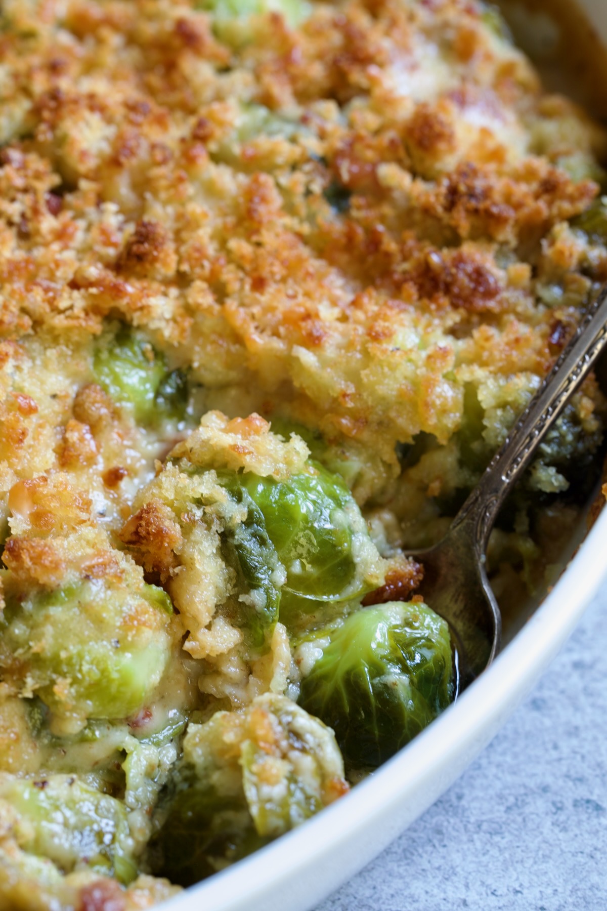 Brussels Sprouts Gratin in oval baking dish with spoon scooping some up.