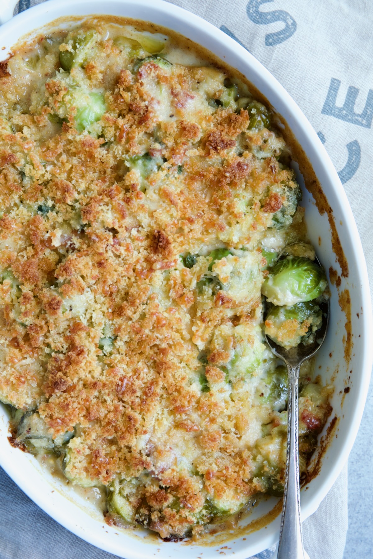 Brussels Sprouts Gratin in oval baking dish with spoon scooping some up.