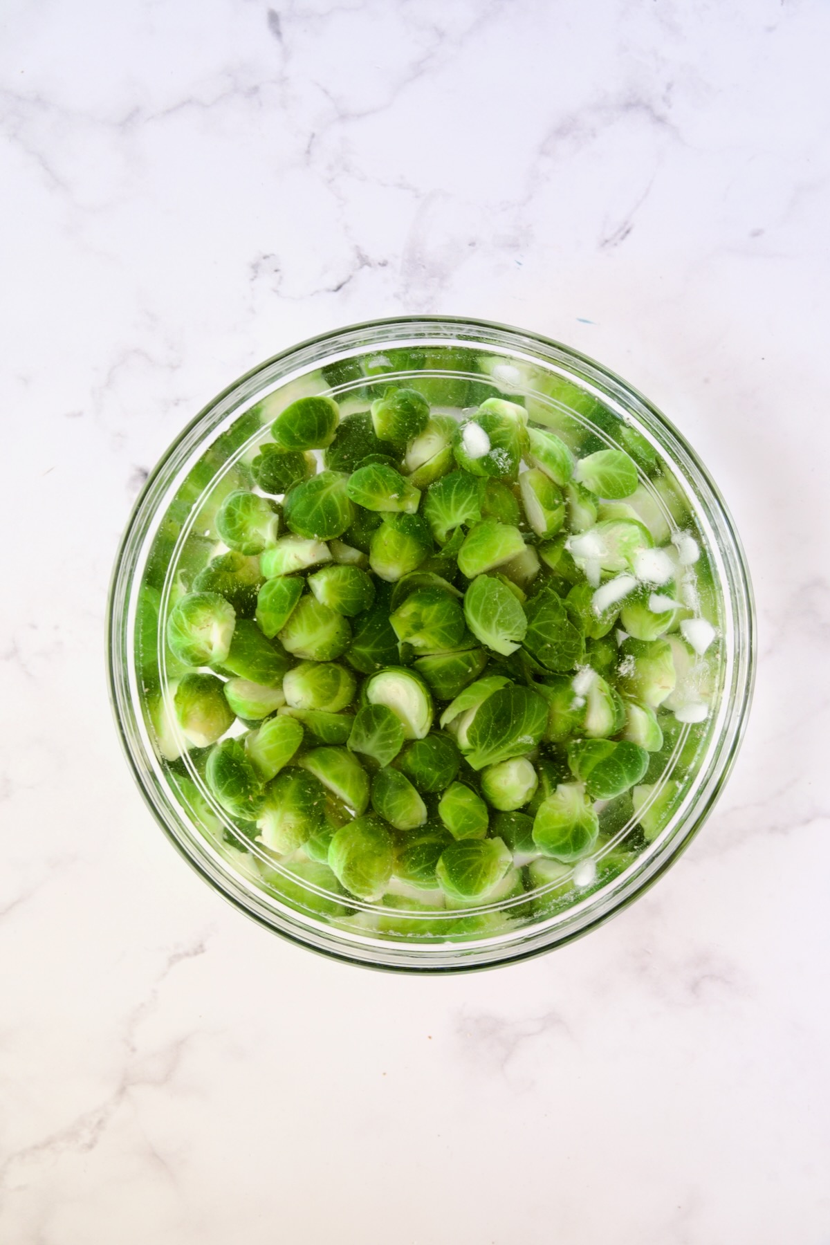 Blanched Brussels sprouts halves in ice bath in glass bowl.