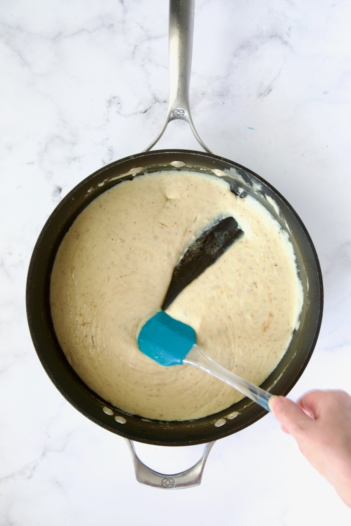 Cheese sauce in nonstick skillet with blue spatula.