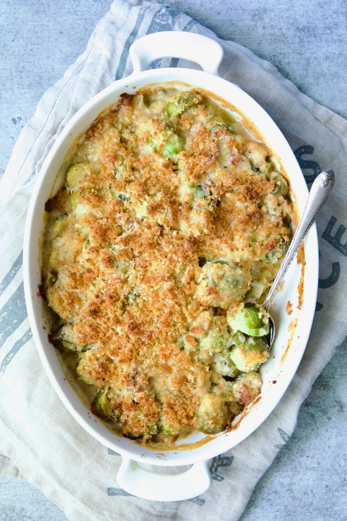 Brussels Sprouts Gratin in oval baking dish with spoon scooping some up.