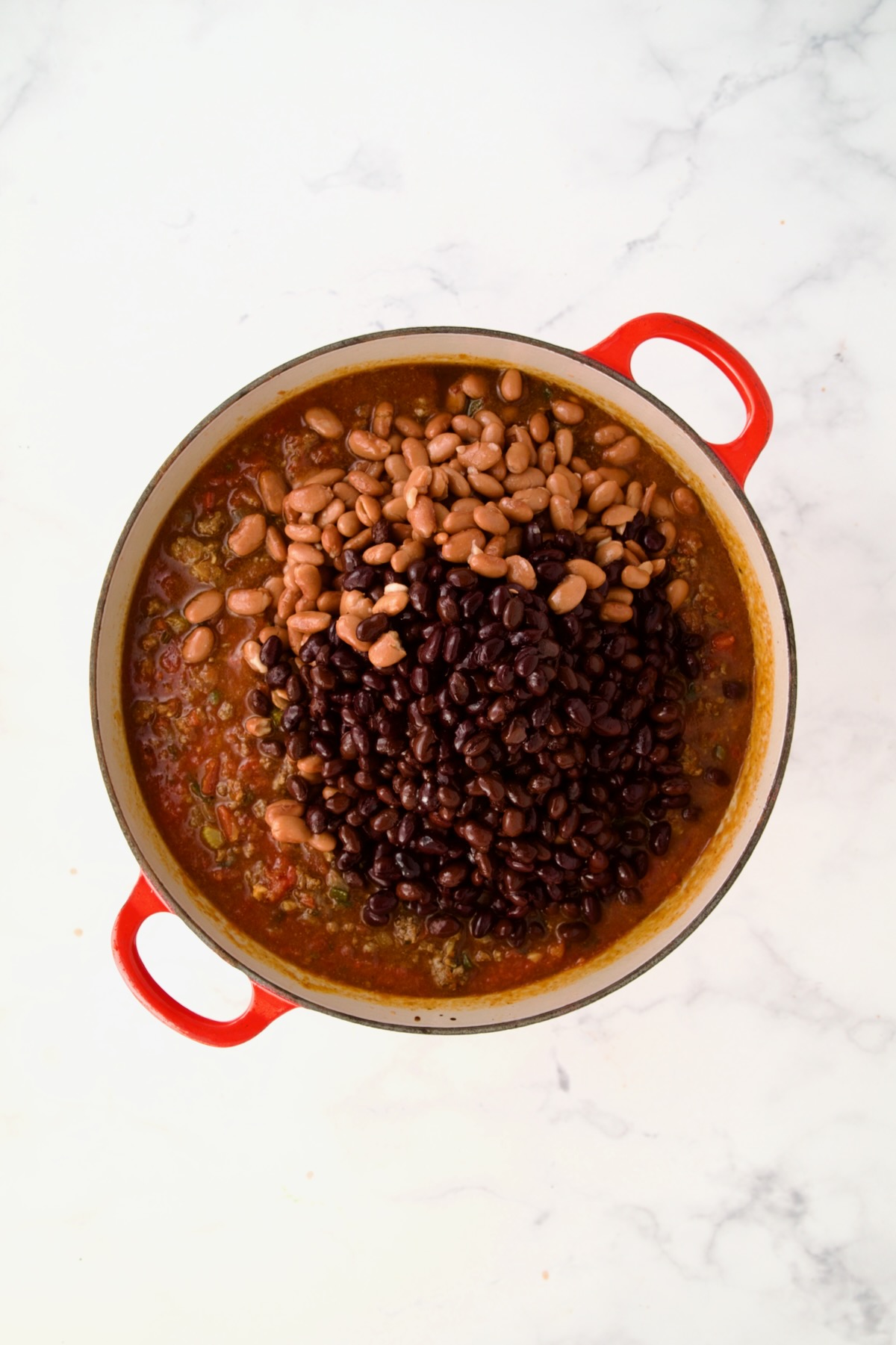 Beans added to chili in process in red Dutch oven.