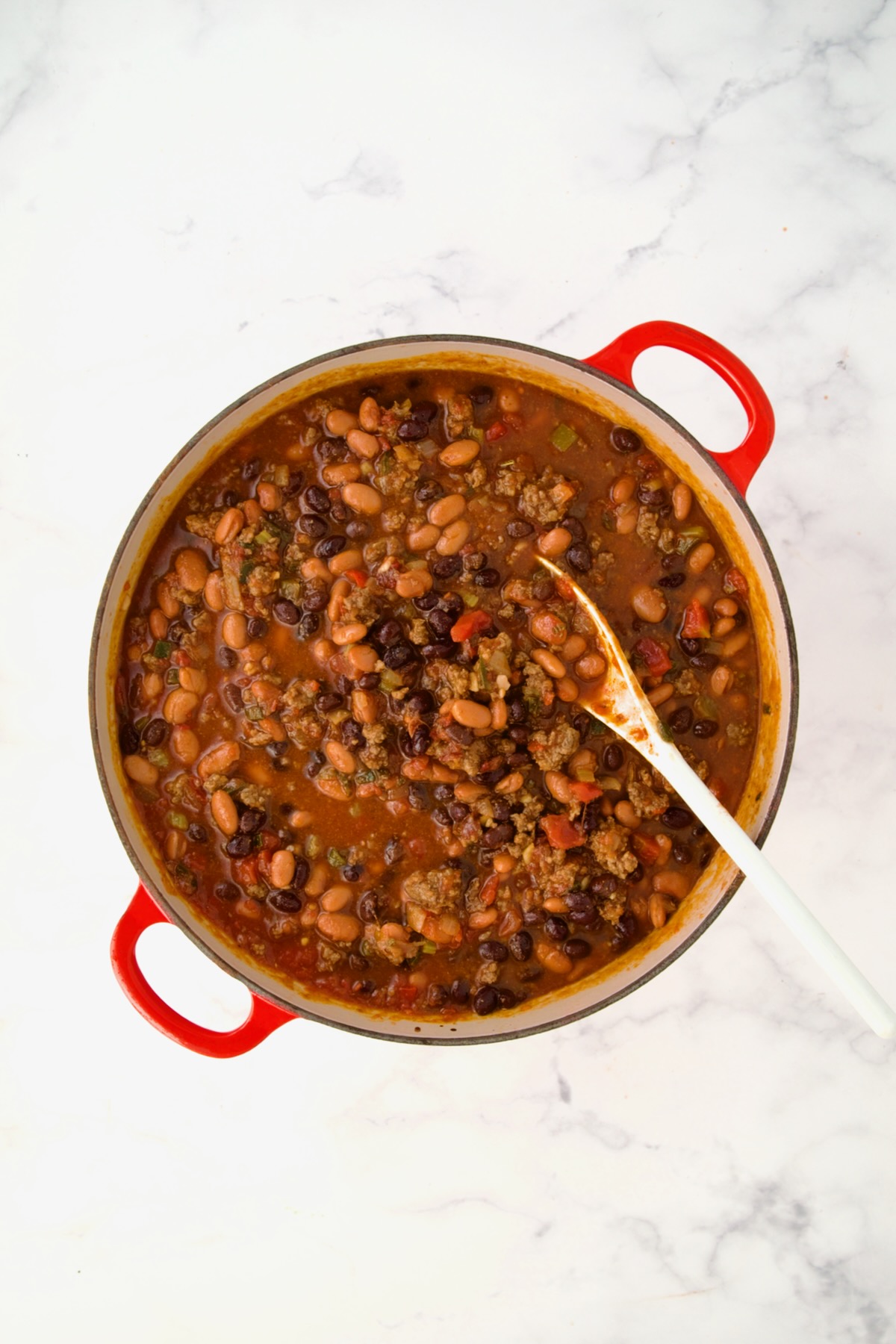 Beans stirred into chili in process in red Dutch oven.
