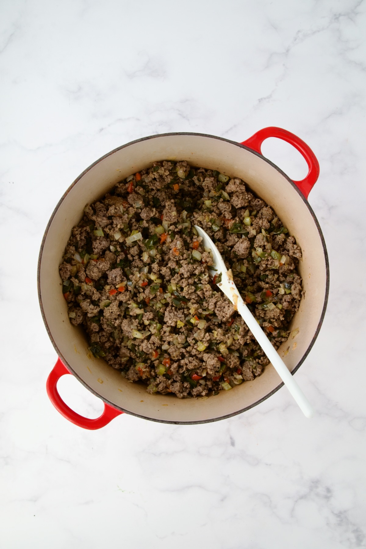Ground beef added to cooked onions, peppers and celery in red Dutch oven.