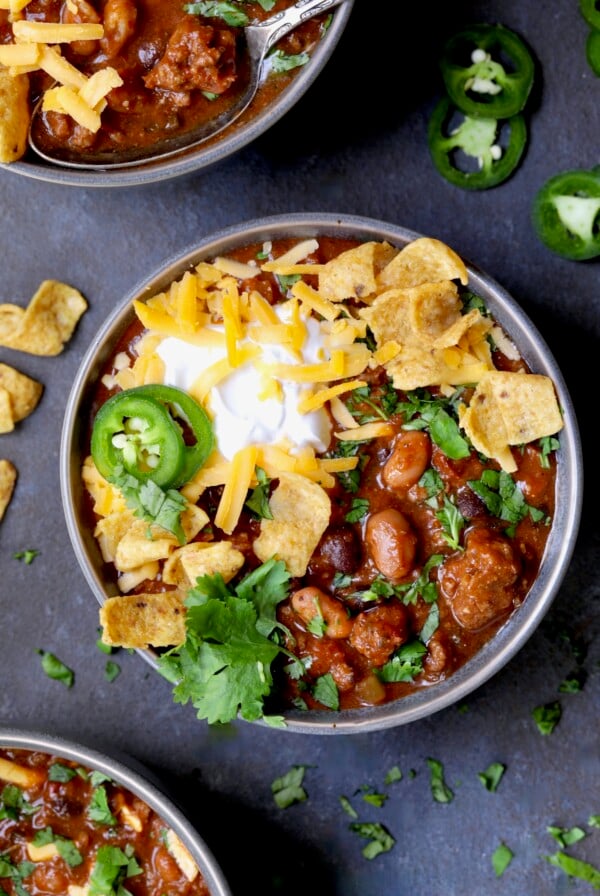 One bowl of Dutch Oven Chili with corn chips, cheese, sour cream jalapeno slices and cilantro in gray bowl.