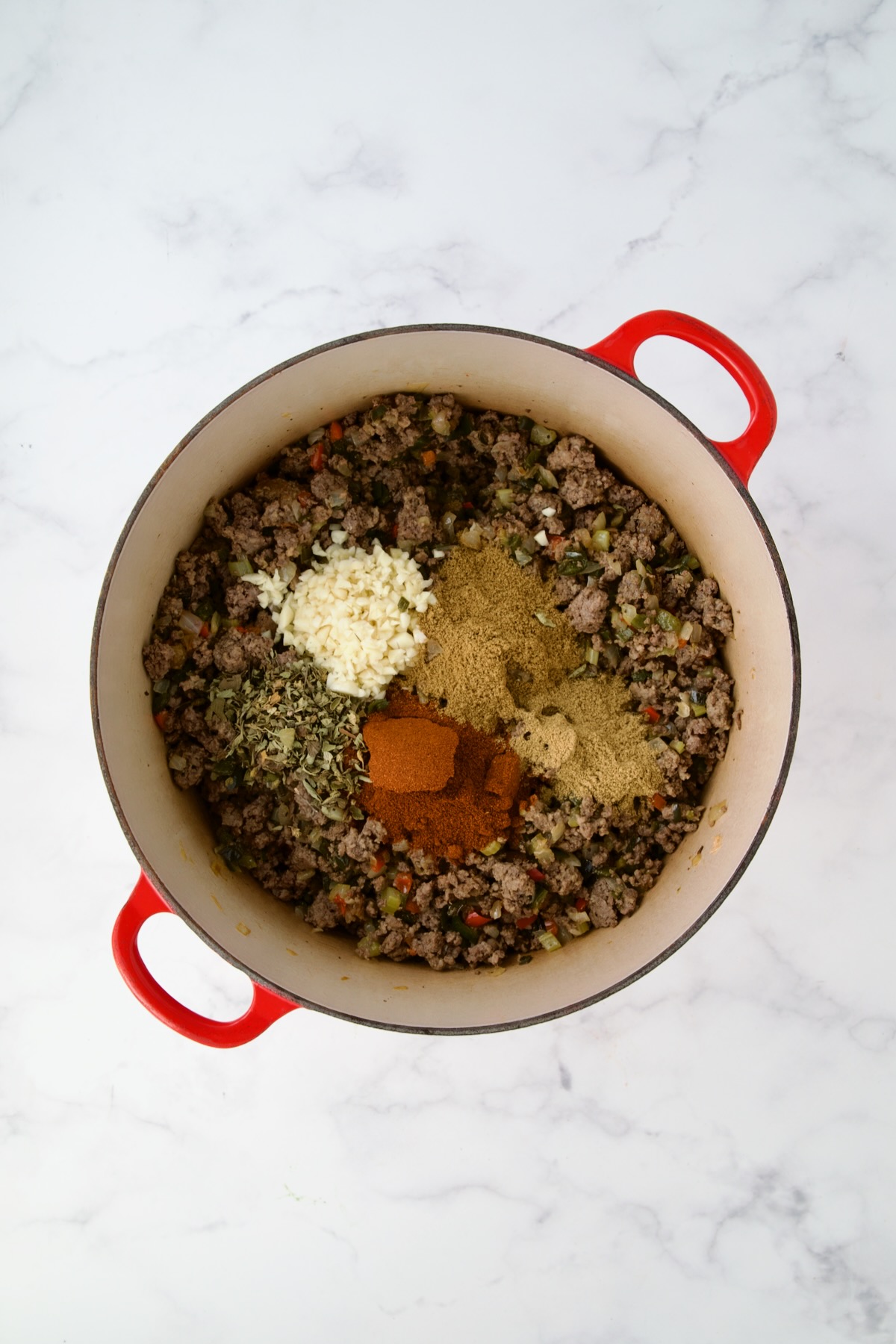 Spices added to ground beef and vegetables in red Dutch oven.