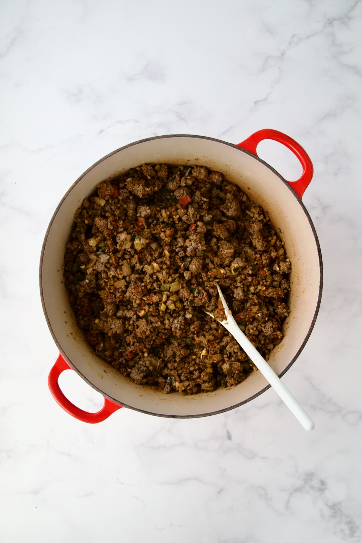 Spices stirred into ground beef and vegetables in red Dutch oven.