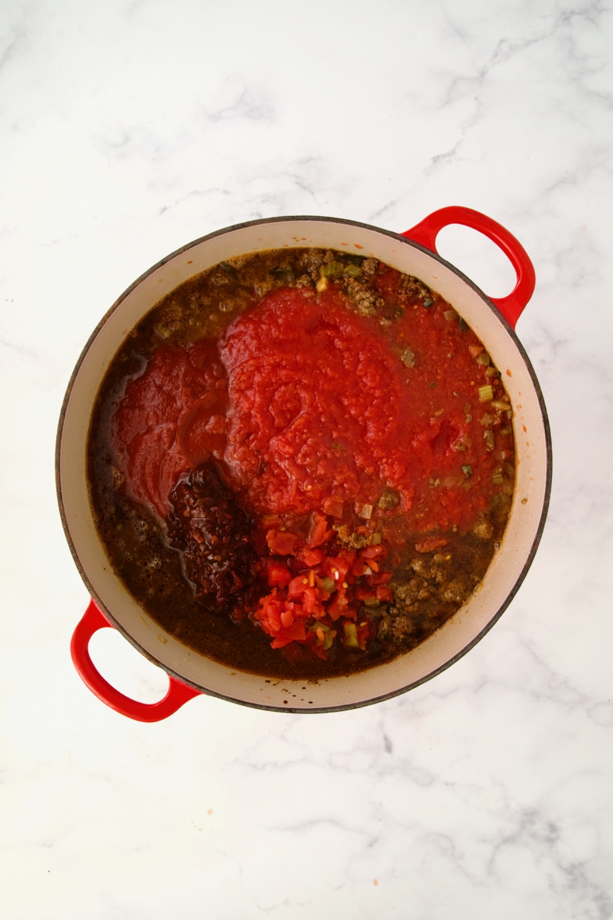 Tomatoes, chipotles, broth and water added to meat and vegetables in red Dutch oven.