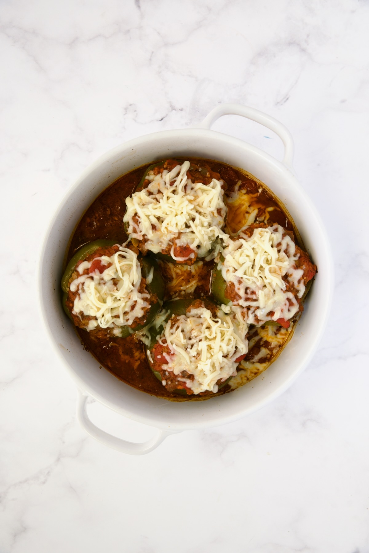 Baked bell peppers in deep white round baking dish with cheese placed on top.